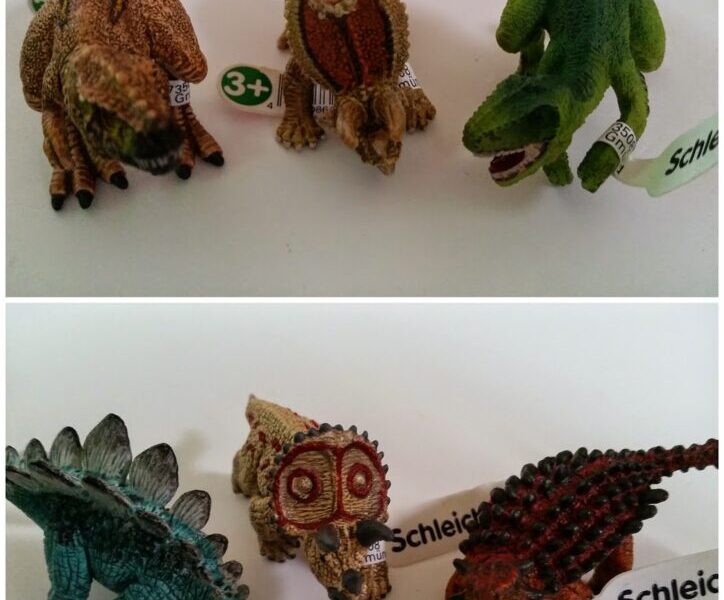 Two rows of toy dinosaur figurines on a white surface. The top row includes brown and green dinosaurs with Schleich tags on their legs. The bottom row shows a blue Stegosaurus, a brown Triceratops skull, and two more dinosaurs with similar tags.