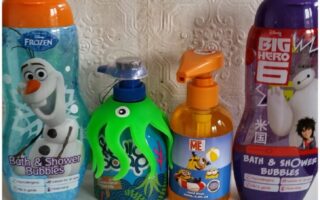 Four bottles of children’s bath products stand side by side. The first has Olaf from Frozen, the second is a green octopus-shaped bottle, the third is orange with Minions, and the fourth is purple with Baymax and Hiro from Big Hero 6. Textured white wall behind.
