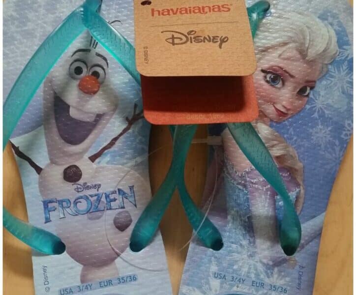 A pair of blue Havaianas flip-flops featuring Disney’s Frozen characters Olaf and Elsa, with snowflake designs. A brown Havaianas Disney tag is attached. The size is UK 3/4, EUR 35/36, and “Frozen” is printed on Olaf’s footbed.