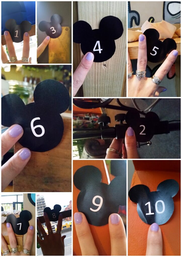 A collage of ten photos shows a hand with lavender nail varnish and rings holding numbered black Mickey Mouse head silhouettes, 1 to 10, against various backgrounds including wood, orange paint, and metal machinery.