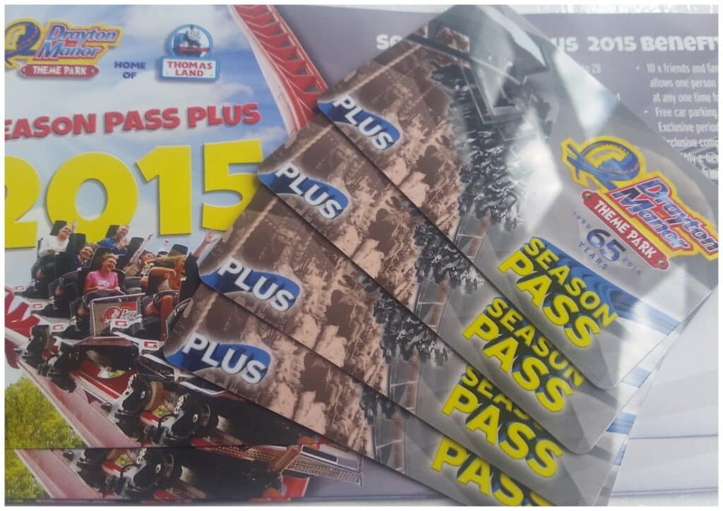 Five Drayton Manor Theme Park 2015 season pass cards are fanned out on top of a brochure featuring a rollercoaster image and the Drayton Manor and Thomas Land logos. The text “Season Pass Plus 2015” is clearly visible.