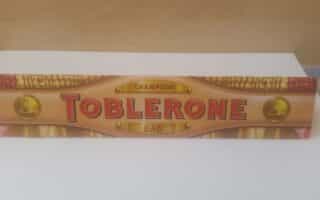 A large Toblerone chocolate bar box with "CHAMPION DAD" written above and below the bold red Toblerone logo, decorated with gold and laurel designs, set against a plain background.