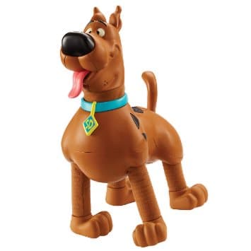 A plastic Scooby-Doo toy figure stands with a happy expression, tongue out and eyes wide. It has brown fur, a blue collar with a yellow diamond-shaped tag, and black spots on its back. The figure’s legs are slightly bent as if in mid-step.