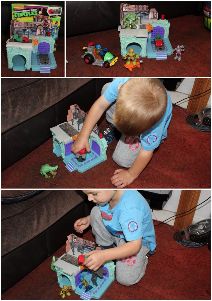 A young child with fair hair plays on a brown carpet with a Teenage Mutant Ninja Turtles playset and figures. The playset has a blue door, brick building, and accessories. The child arranges colourful figures and vehicles on and around the playset.