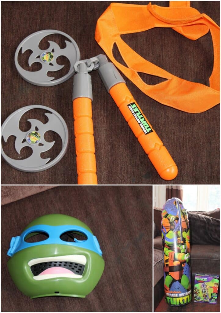 A set of Teenage Mutant Ninja Turtles toys: grey plastic ninja stars, orange nunchaku, orange sash, green turtle mask with a blue band, and a skateboard with colourful Ninja Turtles graphics, all on a brown sofa.
