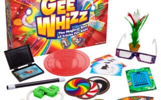 A colourful magic trick set called “Gee Whizz: The Magical Box of Tricks For Kids” is displayed. The box is bright with rainbows and stars. Various magic props are arranged in front: cards, rings, rope, wand, glasses, coins, and other playful accessories.