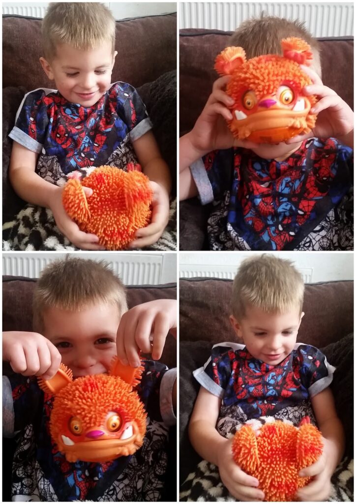 A young boy with short blond hair, wearing a Spider-Man shirt, sits on a sofa holding an orange, fuzzy toy monster with large eyes and teeth. He smiles, plays with, and pretends to wear the toy on his face in four different photo panels.