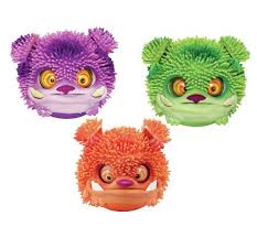 Three round, fuzzy-textured toy monster heads are shown: one purple with yellow eyes and small ears, one green with orange and yellow eyes, and one orange with red ears and yellow eyes. Each has a toothy grin and spiky, rubbery hair.