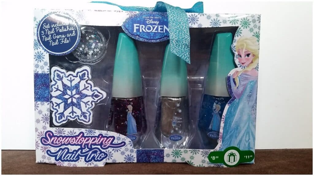 Boxed Disney Frozen nail varnish set labelled “Snowstopping Nail Trio.” The packaging shows Elsa on the right and contains three nail varnishes, a small bag of nail gems, and an emery board. A sparkly blue ribbon is tied at the top. For ages 8 and up.