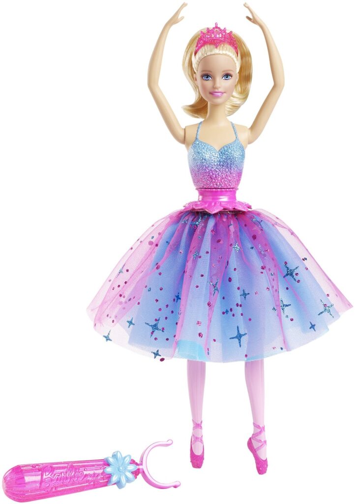 A blonde ballerina doll in a sparkly blue and pink tutu with a pink tiara poses with arms up. She wears pink pointe shoes and has a pink waist ribbon. A pink tool with a blue flower, designed for the doll, lies in front of her.