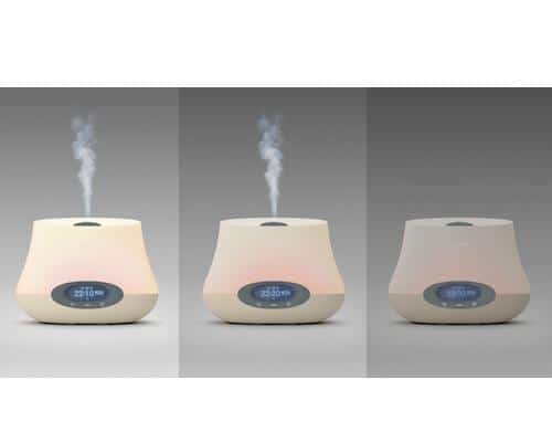 Three beige, dome-shaped humidifiers with digital displays are shown side by side, emitting thin streams of mist from openings on top. The background is a plain gradient grey, and each device appears identical in design and function.