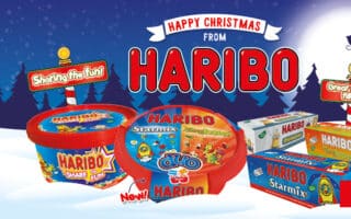 Snowy night scene with a sleigh silhouette flying past a “Happy Christmas from HARIBO” sign. Assorted Haribo sweet tubs and boxes are displayed in front. Signs read “Sharing the fun!” and “Great stocking fillers!” A red “Find out more” button is at the bottom right.
