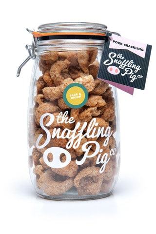 A clear glass jar filled with golden brown pork scratching pieces. The jar is labelled "The Snaffling Pig Co." with a small green badge reading "Sage & Onion." A product tag labelled "Pork Scratchings" hangs from the jar’s sealed metal clasp.