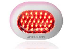 Oval-shaped white and pink device with multiple glowing red LED lights inside. The words "LOVE MY SKIN" are printed on the front below the lights. The device is photographed against a white background.