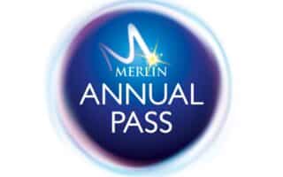 A circular blue logo with a glowing border. In the centre, white text reads "MERLIN ANNUAL PASS," with a stylised "M" and a yellow star above the word "MERLIN." The background fades from dark blue to lighter blue at the edges.