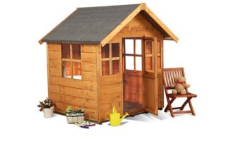 A small wooden playhouse with windows and an open door sits on a white background. Nearby are a wooden chair with a teddy bear, a yellow watering can, toy gardening tools, potted flowers, and a basket, suggesting a playful, garden-themed setting.