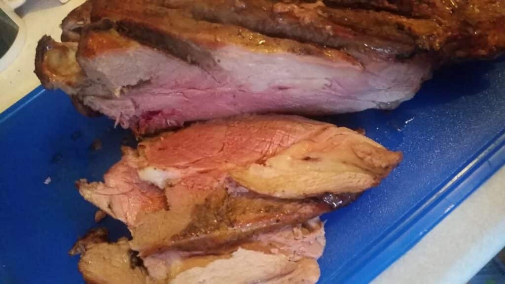 A close-up of a partially sliced roast beef on a blue chopping board. The meat has a browned, seasoned crust and a juicy, pink interior with visible marbling. Two thick slices lie in front of the main portion, showing tender, cooked texture.