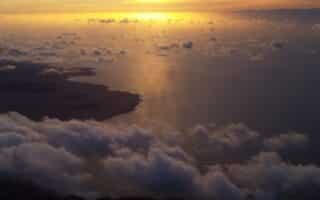 An aeroplane wing and clouds above the water.