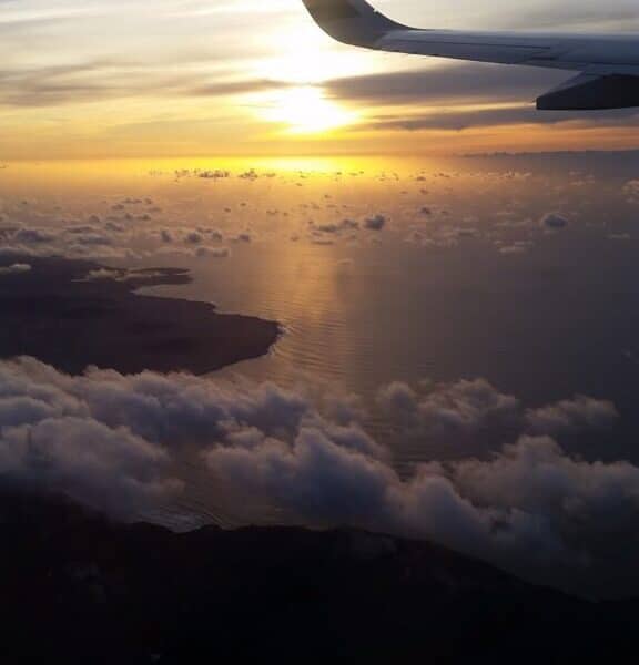An aeroplane wing and clouds above the water.