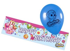 A blue balloon with a "Shopkins" seal character floats above a colourful "Shopkins" birthday banner. The banner features "HAPPY BIRTHDAY" in bold letters, surrounded by cartoon food characters, gifts, and festive decorations.