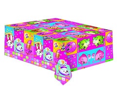 A rectangular gift box is wrapped in colourful, cartoon-themed wrapping paper featuring various Shopkins characters on pink, blue, and green backgrounds with confetti patterns and playful squares along the edges. A small piece of wrapping paper hangs down.
