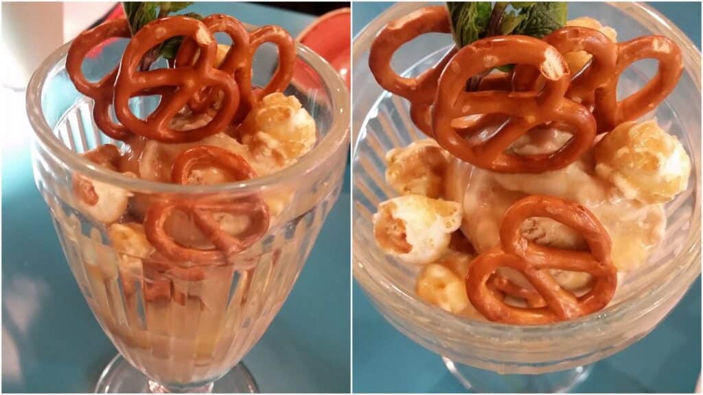 A glass sundae dish filled with caramel popcorn and mini pretzels, topped with a drizzle of caramel sauce and a small sprig of mint, shown from two close-up angles on a blue table-top.