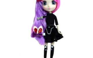 A fashion doll with large blue eyes, pink and purple long hair, and decorative hair clips. She wears a black crop top, black skirt with chains, and black knee-high socks with white bows. The background is plain white.