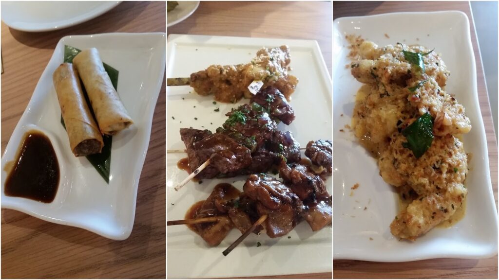 A trio of dishes: left shows two spring rolls with dipping sauce; centre has skewers of grilled meat with herbs; right features battered, seasoned fried prawns garnished with herbs, all served on white plates atop a wooden table.