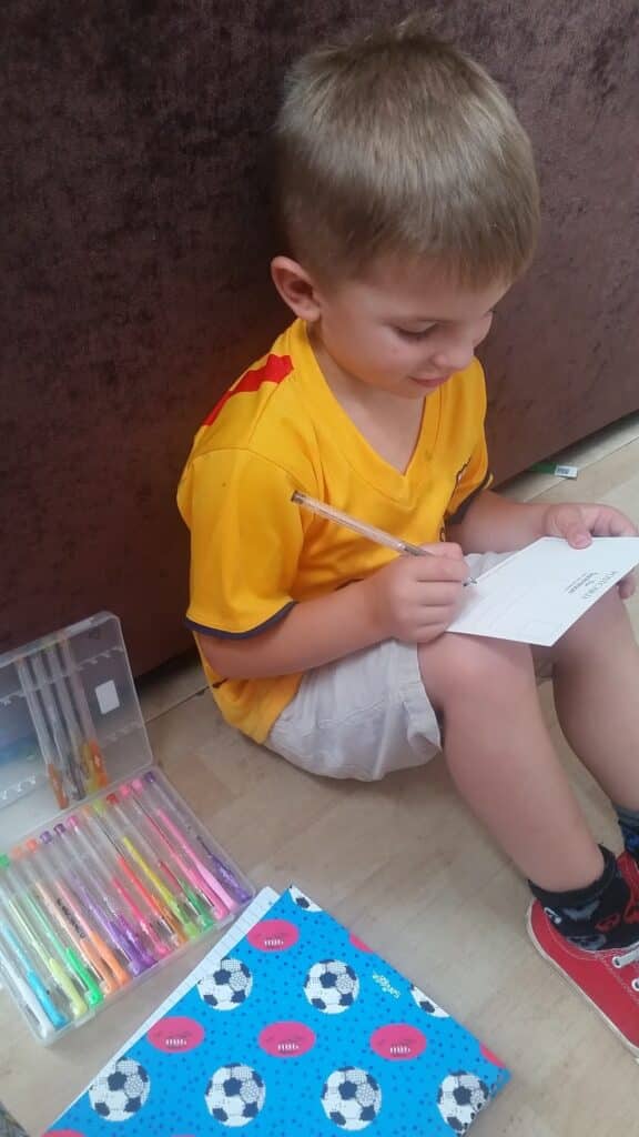 A boy sitting on the floor writing on a piece of paper.