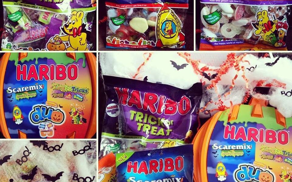 A collage of Halloween-themed Haribo sweet packs, including “Trick or Treat,” “Scaremix,” and “Tangfastricks.” The sweets are surrounded by fake cobwebs, plastic spiders, and Halloween decorations like “Boo!” text and bat shapes.