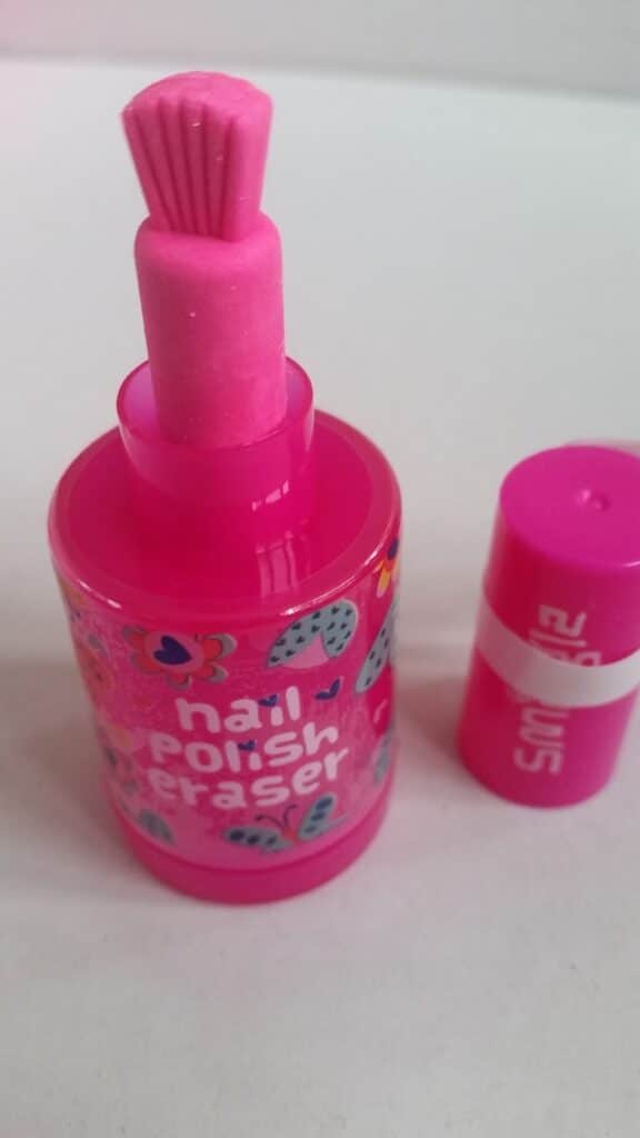 A bright pink, cylindrical object resembling a nail varnish bottle, but it is actually a rubber shaped like a nail varnish bottle. The cap is off, revealing the pink rubber shaped like a brush. The label reads "nail varnish rubber" with heart and flower designs.