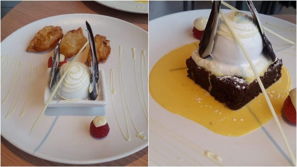 Two plates of elegant desserts: the left plate has a white mousse dome with chocolate shards, golden fritters, raspberries, cream dots, and white chocolate drizzles. The right plate shows a similar mousse atop a brownie, with yellow sauce, chocolate shards, and a raspberry.