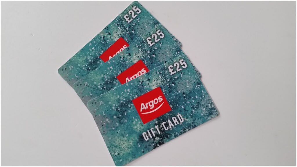 Three Argos gift cards, each valued at £25, are fanned out on a white surface. The cards have a speckled turquoise design with the red Argos logo and "GIFT CARD" written in white.