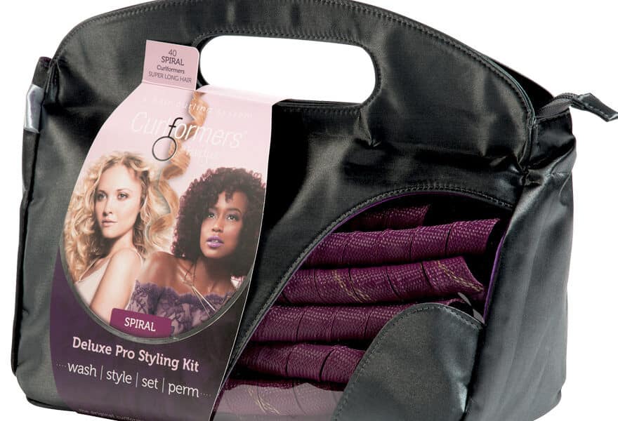 A black carrying case with a handle, containing a purple Curlformers Deluxe Pro Styling Kit. The packaging shows two women with curly hair and includes text: “Deluxe Pro Styling Kit—wash | style | set | perm.” The spiral curlers are visible inside the case.