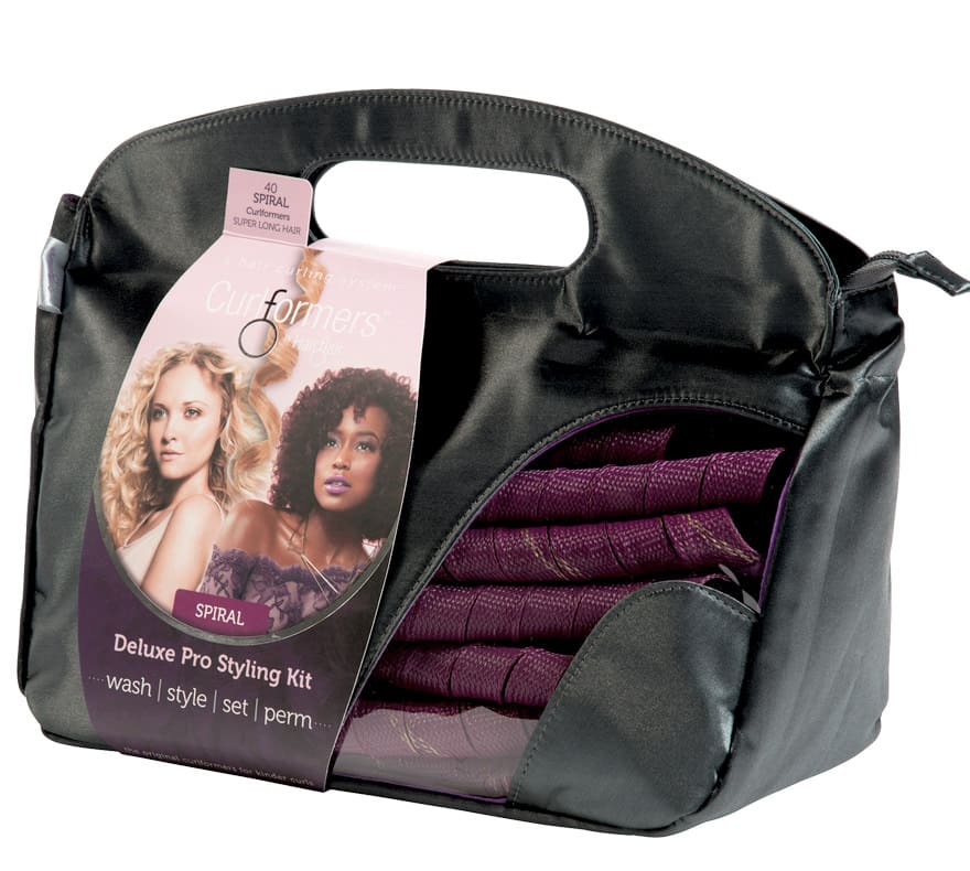 A black carrying case with a handle, containing a purple Curlformers Deluxe Pro Styling Kit. The packaging shows two women with curly hair and includes text: “Deluxe Pro Styling Kit—wash | style | set | perm.” The spiral curlers are visible inside the case.