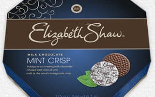 Octagonal box of Elizabeth Shaw Mint Crisp Milk Chocolate. The dark blue packaging displays two chocolate discs, one partly unwrapped, with a mint leaf beside them. Text highlights the 175g weight and describes milk chocolate with mint oil and honeycomb crisp.