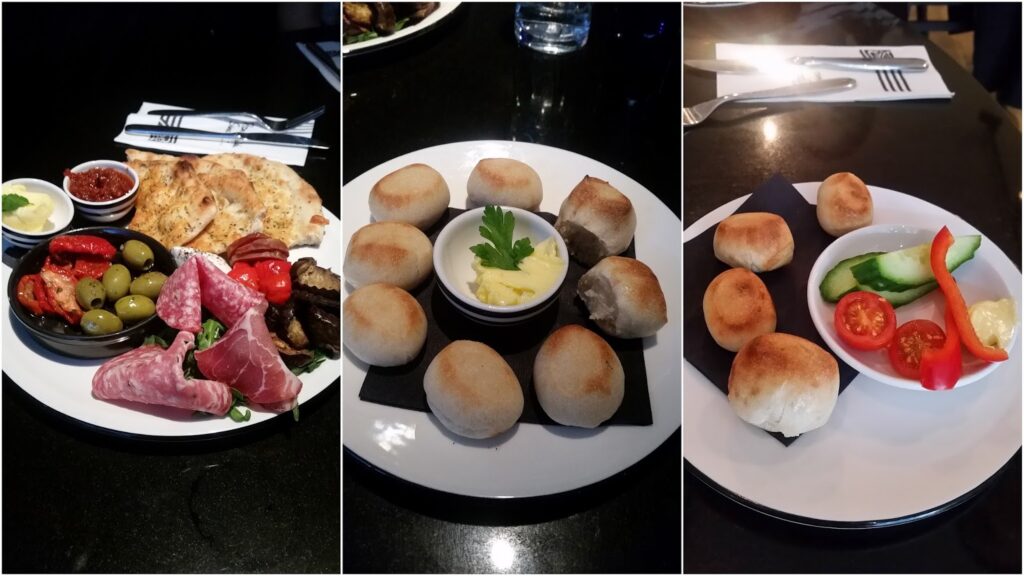 A collage of three plates: left plate with cured meats, olives, grilled vegetables, flatbread, and dip; centre plate with dough balls and a small dish of butter; right plate with dough balls, sliced cucumber, tomatoes, pepper, and a dollop of dip.
