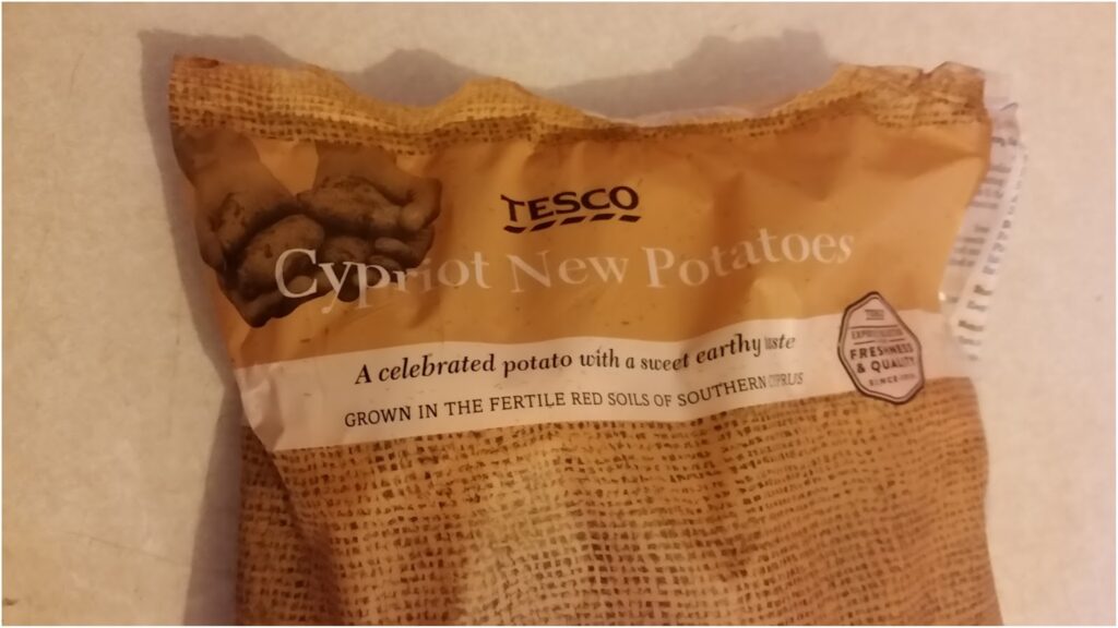 A brown bag of Tesco Cypriot New Potatoes with text reading: "A celebrated potato with a sweet earthy taste. Grown in the fertile red soils of Southern Cyprus." The packaging has an image of potatoes and a freshness and quality seal.