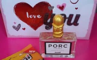 A gift set on a pink surface features a card reading “I really really really love you” with hearts, a bottle of PORC perfume with a gold pig-shaped cap, and a pack of Peperami Snack Pack with cartoon sausages on the packaging.