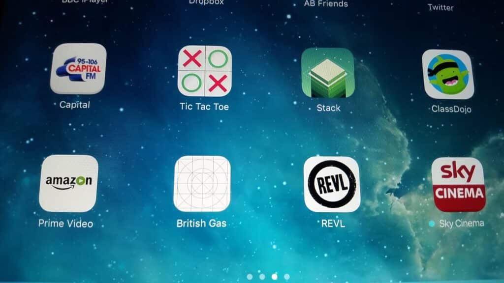 A tablet home screen displays eight app icons: Capital, Noughts and Crosses, Stack, ClassDojo, Prime Video, British Gas, REVL, and Sky Cinema, all arranged in two rows on a blue starry background. The icons are colourful and clearly labelled.