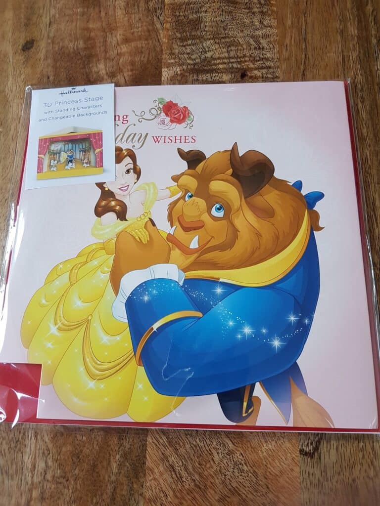A greeting card featuring Belle and the Beast from Disney's "Beauty and the Beast" dancing together. Belle wears a yellow dress, the Beast a blue coat. A sticker advertises a "3D Princess Stage" with stand-up characters inside. The card is on a wooden surface.