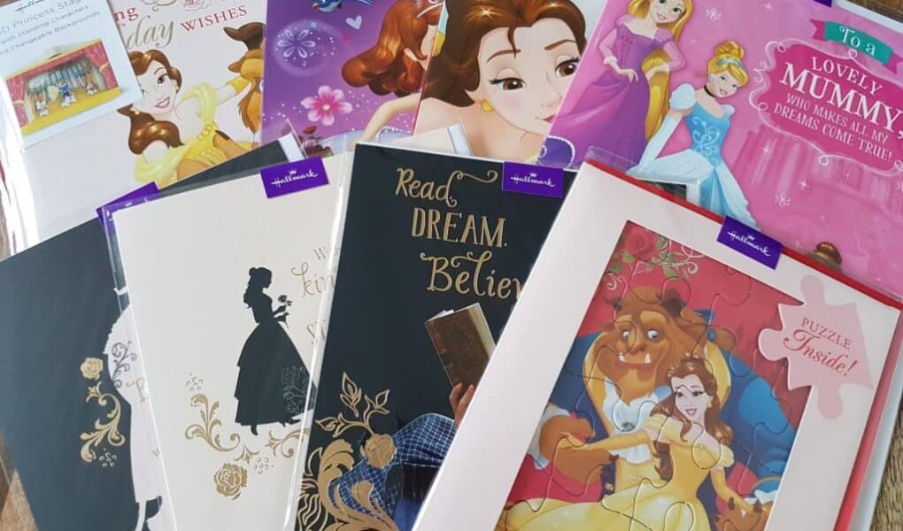 A collection of Hallmark cards and a puzzle featuring Disney princesses and characters, including Belle from Beauty and the Beast, and multiple princess-themed designs, arranged in an overlapping display on a wooden surface.