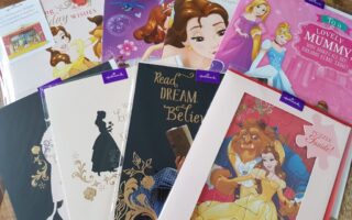 A collection of Hallmark cards and a puzzle featuring Disney princesses and characters, including Belle from Beauty and the Beast, and multiple princess-themed designs, arranged in an overlapping display on a wooden surface.