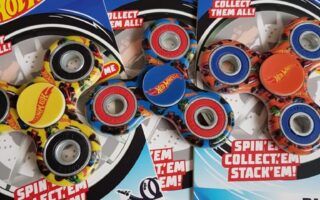 Three Hot Wheels-branded Bladez Spinnerz fidget spinners in packaging are shown. Each pack features a yellow sports car image, Hot Wheels logos, and colourful spinners with car-themed designs on a blue and white background.
