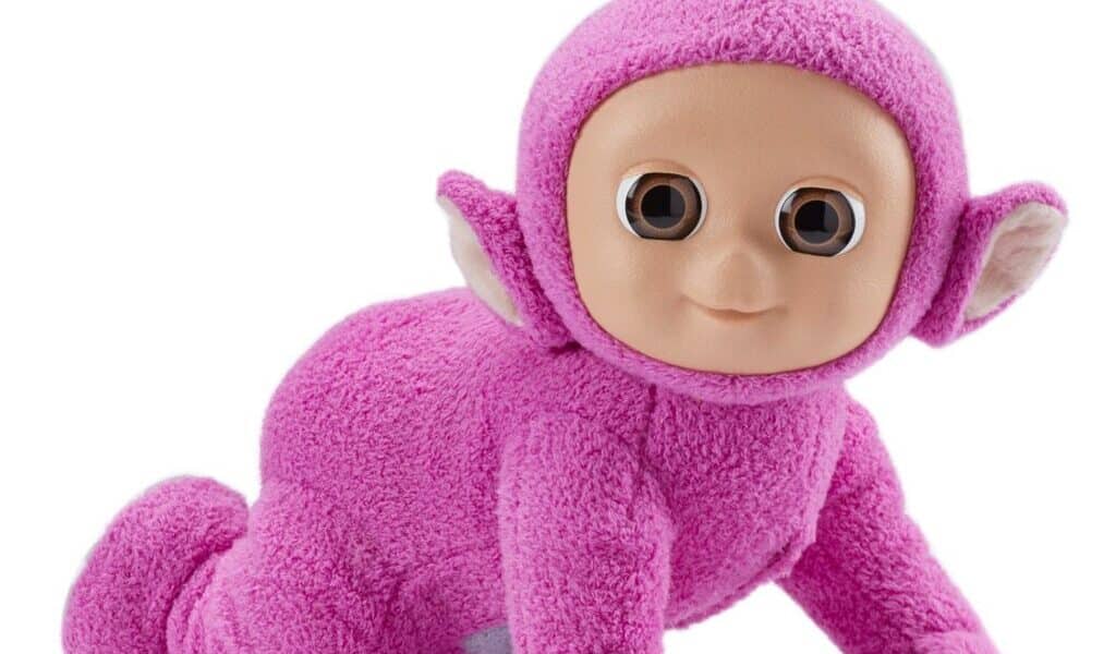 A cuddly toy resembling a cartoonish humanoid creature with bright pink fuzzy fabric, large round brown eyes, pointy ears, a tan plastic face, and a small round aerial on its head, posed crawling on all fours against a white background.