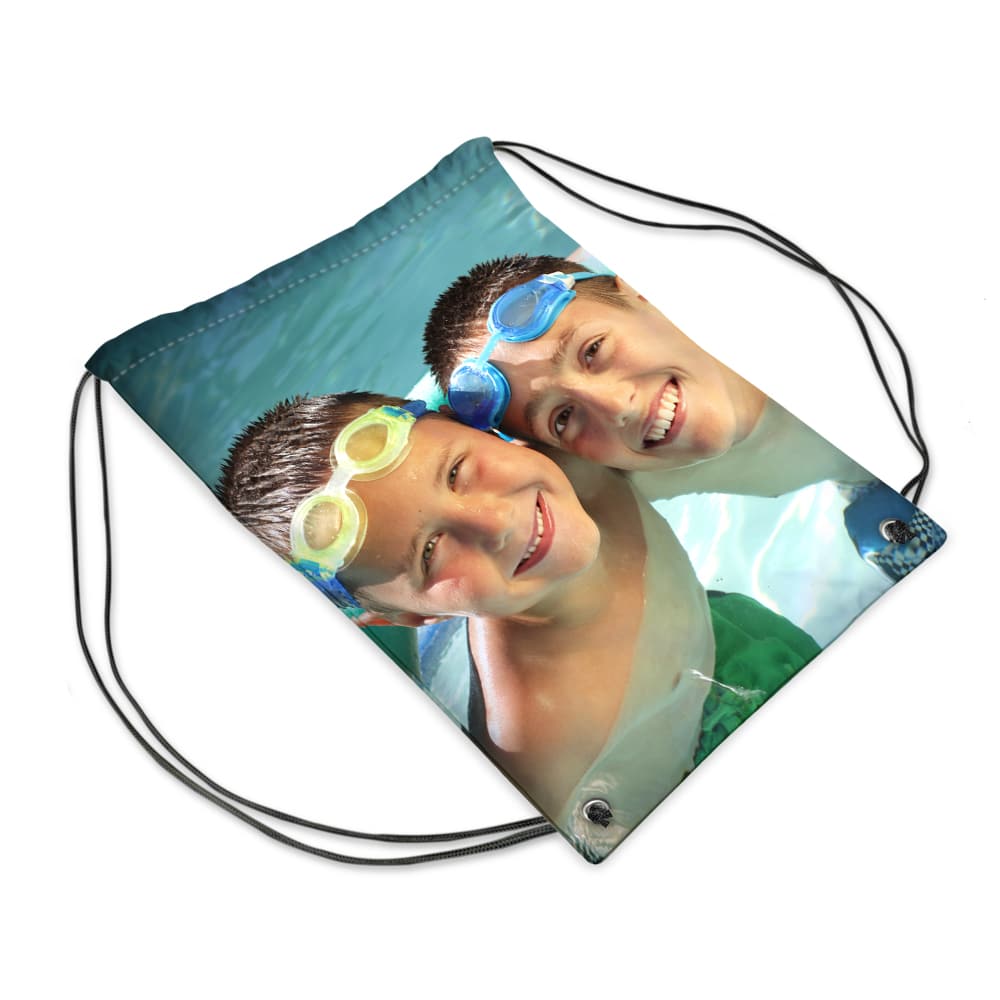 A drawstring bag printed with a photo of two smiling boys in a swimming pool, wearing colourful swim goggles, with their faces close together and water around them. The bag’s strings are black and the image covers the entire front panel.