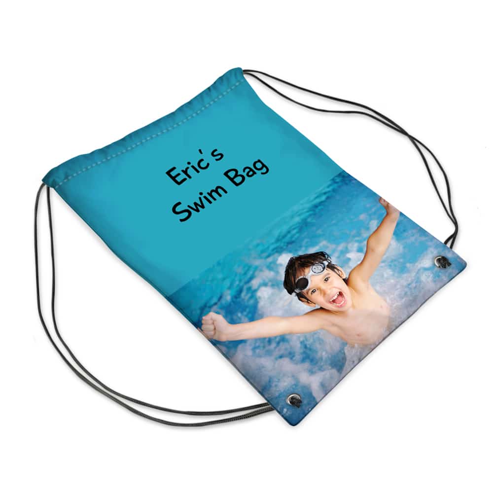 A blue drawstring swim bag featuring black cords, the text “Eric’s Swim Bag” in playful black font, and a photo of a smiling boy wearing swimming goggles, swimming and raising his arms in a pool with splashing water.