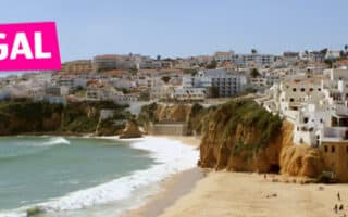 A coastal town in Portugal with white buildings clustered on cliffs above a sandy beach. The turquoise sea curves along the shore, and a pink "PORTUGAL" label is placed on the upper left side of the image.