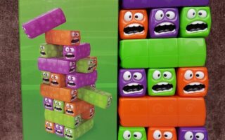 A boxed toy called "Chad Valley Wobbly Worms" stands next to its assembled blocks. The colourful orange, green, and purple blocks are stacked in a tower; each has cartoonish eyes and mouths expressing surprise or worry. The toy is for ages 3 and up.