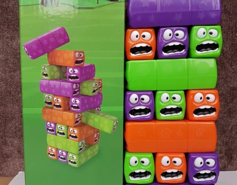 A boxed toy called "Chad Valley Wobbly Worms" stands next to its assembled blocks. The colourful orange, green, and purple blocks are stacked in a tower; each has cartoonish eyes and mouths expressing surprise or worry. The toy is for ages 3 and up.